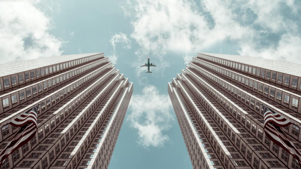 An airplane in the sky (Photo by Jacoby Clarke: https://www.pexels.com/photo/worm-s-eye-view-photo-of-plane-between-two-high-rise-buildings-1307158/)